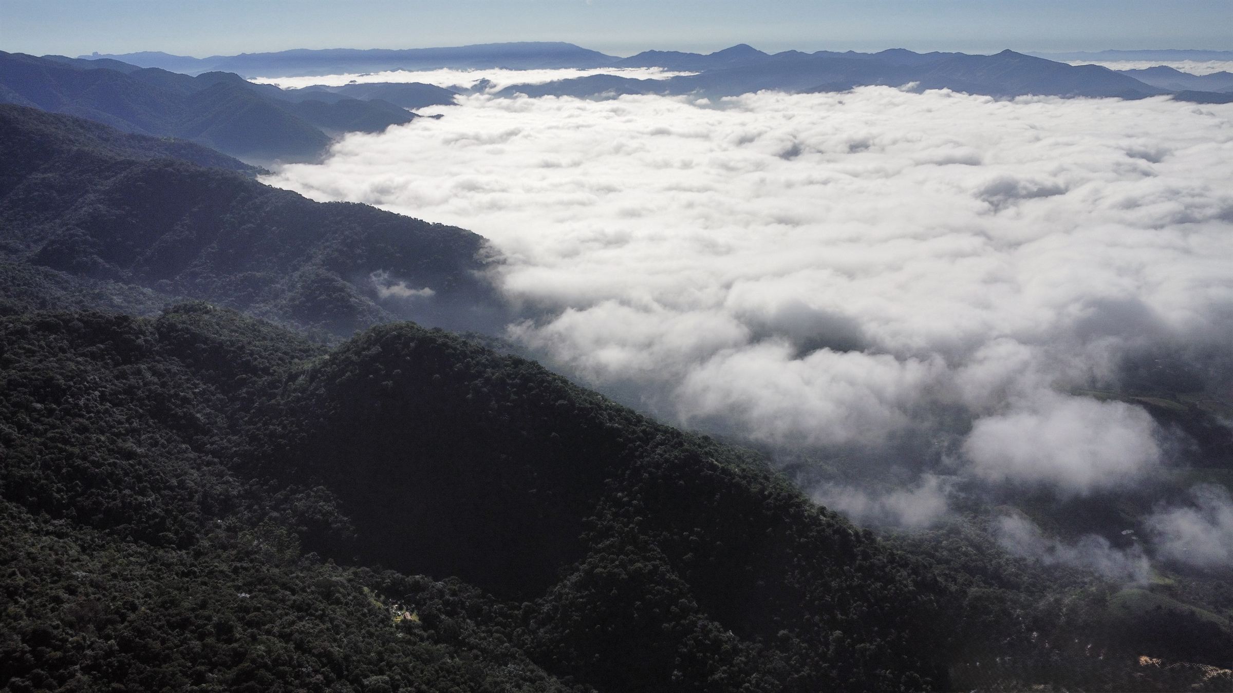 A sea of clouds filling the valley below the mountain, ridgelines fading into the horizon